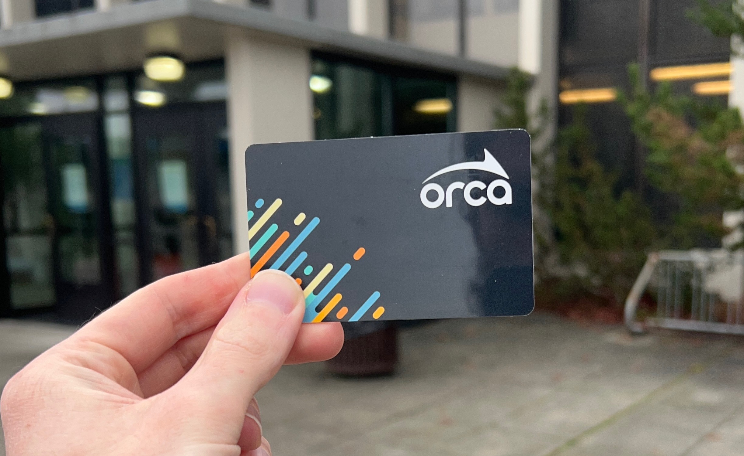View of a hand holding up an ORCA card being held up in front of Building 6 at Highline College